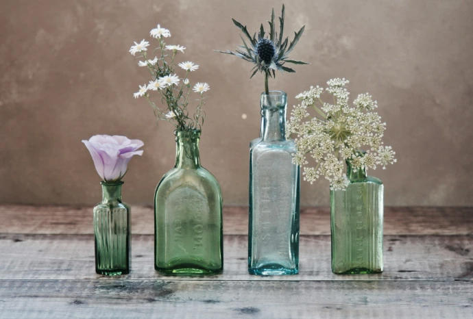 three green and one blue glass vases with flowers inside
